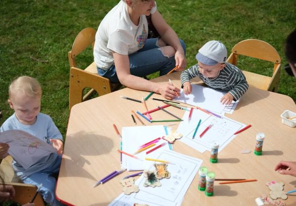 Children and parents engaging in outdoor art and craft activities with colored pencils.