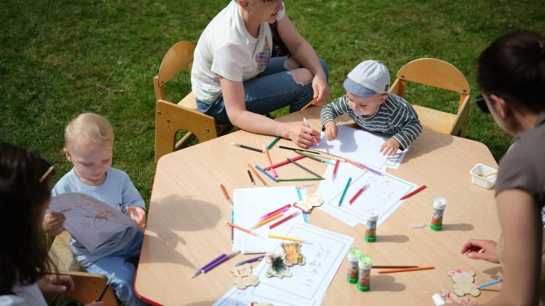 Children and parents engaging in outdoor art and craft activities with colored pencils.