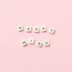Scrabble tiles spelling 'Happy Mind' on a pink background, flat lay.