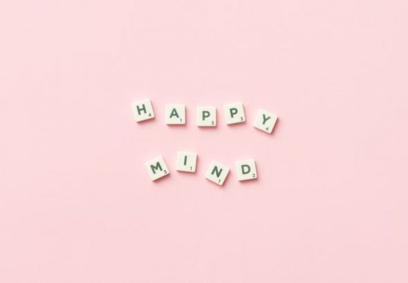 Scrabble tiles spelling 'Happy Mind' on a pink background, flat lay.