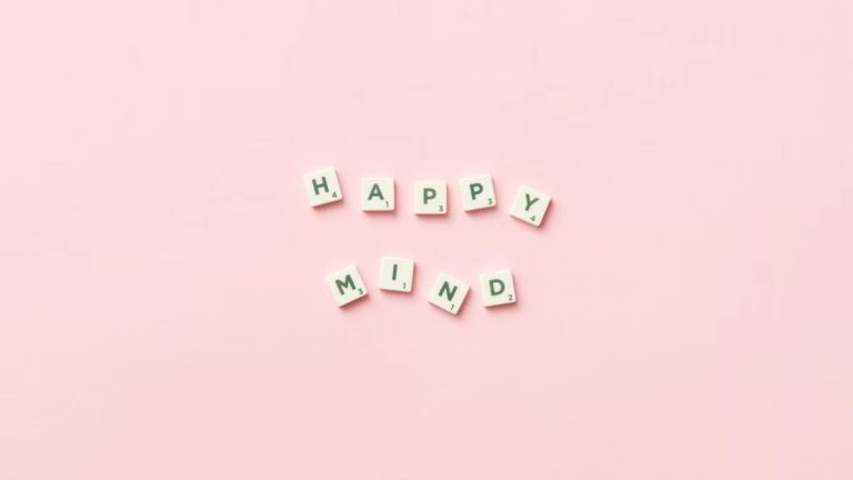 Scrabble tiles spelling 'Happy Mind' on a pink background, flat lay.
