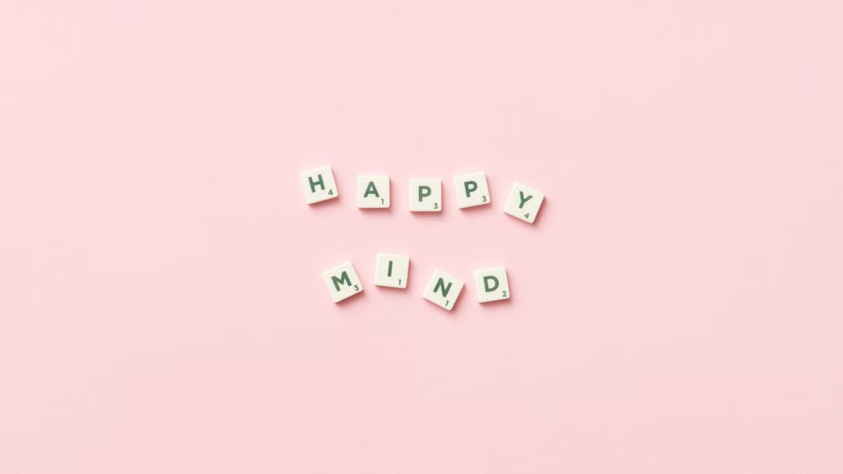 Scrabble tiles spelling 'Happy Mind' on a pink background, flat lay.